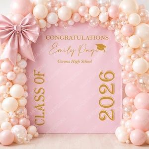 May include: A pink graduation backdrop with a large bow and balloon arch. The backdrop reads "Congratulations Emily Page Corona High School Class of 2026" in gold lettering. The balloons are pink, white, and clear.