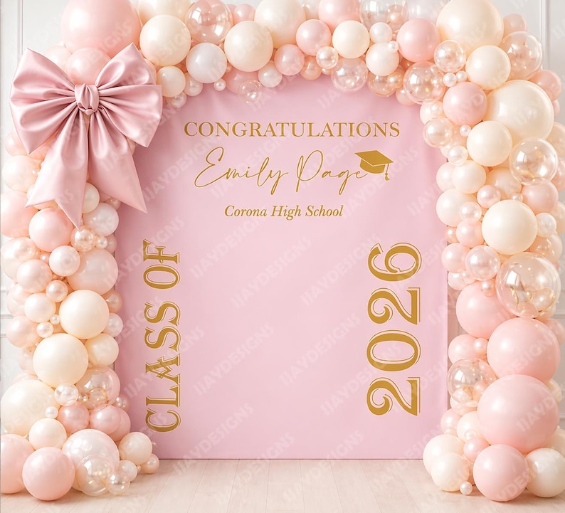 May include: A pink graduation backdrop with a large bow and balloon arch. The backdrop reads "Congratulations Emily Page Corona High School Class of 2026" in gold lettering. The balloons are pink, white, and clear.