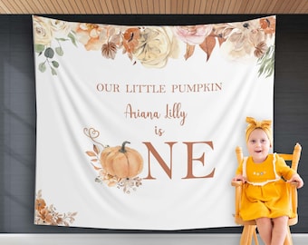Könnte beinhalten: Ein weißer Hintergrund mit einem Aquarell-Blumenmuster und dem Text "Our Little Pumpkin Ariana Lilly is One" mit einem großen orangefarbenen Kürbis und einem kleinen Kind in einem gelben Kleid, das auf einem Holzstuhl sitzt.