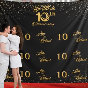 May include: A black backdrop with gold glitter and the text "We still do 10th Anniversary" with the names "Lisa & Richard" repeated multiple times. A couple are standing in front of the backdrop.