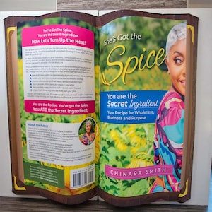 Puede incluir: Un libro abierto con el título "She's Got the Spice" y el subtítulo "You are the Secret Ingredient". La portada presenta a una mujer con cabello gris y una blusa colorida. Las páginas del libro contienen texto y una foto de la autora.