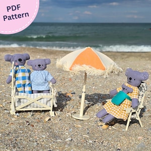 May include: A PDF pattern for fabric koala dolls featuring two standing koalas in a small striped crib, one sitting in a beach chair holding a smaller koala, and an orange and white fringed beach umbrella. The dolls wear checkered and dotted outfits.