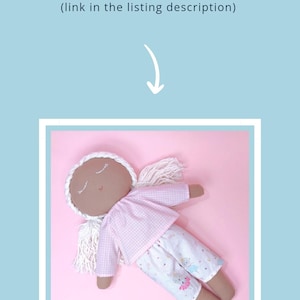 May include: A handmade doll with brown skin, closed eyes, and white yarn hair. The doll is wearing a pink and white gingham shirt and white pants with a pink and blue print. The doll is lying on a pink background.