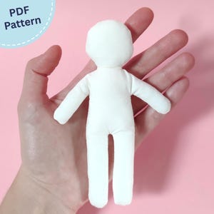 May include: A small, white, blank fabric doll with a rounded head, simple torso, arms, and legs. The doll features a plain, featureless design. The text "PDF Pattern" is visible in the upper left corner of the image.
