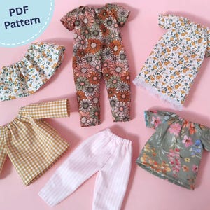 Può includere: Una collezione di vestiti per bambole che include una tuta floreale, un vestito bianco a fiori con bordo in pizzo, un top a quadretti gialli, un paio di pantaloni a righe rosa chiaro, un top floreale e una gonna bianca a fiori. Testo PDF Pattern.