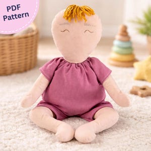 May include: A fabric doll with a pale peach complexion, embroidered facial features, and mustard yellow yarn hair. The doll wears a short-sleeved, dark pink romper. A circular pink badge in the top left corner displays the text PDF Pattern.