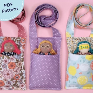 Könnte beinhalten: Drei Puppenschlafsäcke aus Stoff mit langen Schulterriemen. Die linke Tasche hat ein rosa Blumenmuster, die mittlere Tasche ist lila mit weißen Punkten und die rechte Tasche zeigt ein Zitronenmuster mit einer Puppe, die eine gelbe Schlafmaske trägt.