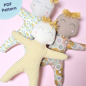 Op de afbeelding: Drie handgemaakte stoffen poppen met geborduurde gezichten en geel garen haar. Eén pop heeft een geel-wit ruitpatroon, een andere heeft witte stof met een gele bloemenprint en de derde heeft een bloemenpatroon met madeliefjes.