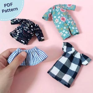 Może przedstawiać: Cztery miniaturowe ubranka dla lalek, w tym ciemny top w kwiaty, turkusowy kombinezon w kwiaty, niebiesko-biała spódnica w paski oraz granatowo-biały top w kratę. Obraz zawiera tekst PDF Pattern w lewym górnym rogu.