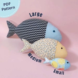 Może przedstawiać: Trzy pluszowe ryby oznaczone jako Large, Medium i Small. Duża ryba ma czarno-biały korpus w jodełkę i jasnoniebieską głowę w kropki. Średnia ryba ma kwiatowy korpus i żółtą głowę w paski. Mała ryba posiada nadruk w cytryny.