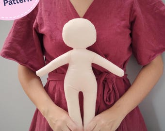 May include: A light beige fabric doll with a round head, outstretched arms, and legs, featuring a smooth, featureless surface. A circular pink badge in the upper left corner contains the white text PDF Pattern.