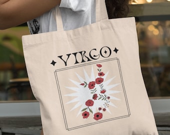 May include: Beige tote bag featuring the word "VIRGO" in a black, stylized font, with a floral design of red flowers and green leaves. The design includes a sunburst and a black border. The bag is carried over the shoulder.