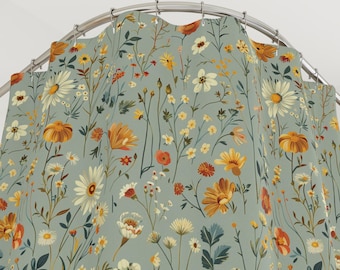 May include: A shower curtain with a floral pattern. The curtain features a light blue background with a repeating pattern of various wildflowers in shades of yellow, orange, white, and green. The curtain is hanging from a curved metal rod.