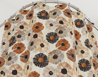 May include: A shower curtain with a repeating floral pattern. The flowers are in shades of brown, orange, and beige, with dark brown centers. The curtain hangs from a curved, silver-colored shower rod. The overall design has a retro, vintage aesthetic.