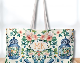 May include: Cream tote bag with a floral and bird design. The bag features blue lanterns, pink and peach flowers, and two blue birds. The initials "MK" are in a cloud-shaped frame. The bag has white rope handles.
