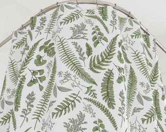 May include: White shower curtain with a repeating pattern of green and grey botanical illustrations, including ferns and other leafy plants. The curtain hangs from a curved, silver-coloured shower rod.
