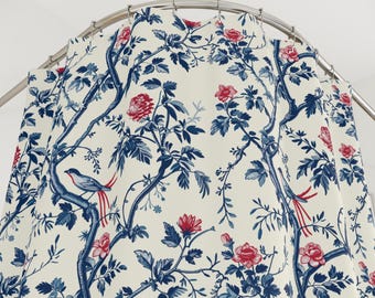 May include: A shower curtain with a botanical design. The curtain features a cream background with blue branches, leaves, and birds, and red flowers. The curtain is hanging from a curved, silver-colored shower rod.
