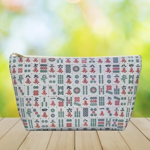 May include: White zippered pouch with a repeating pattern of mahjong tiles. The tiles are white with red, green, and black markings. The pouch is ideal for storing small items.