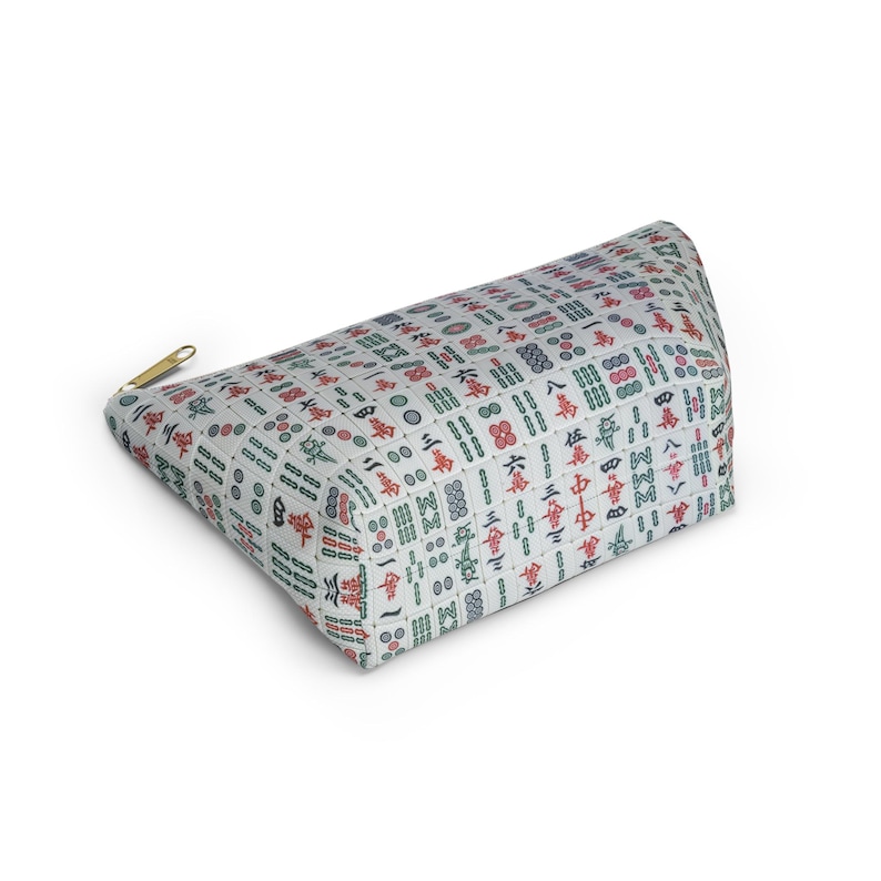 May include: A white zippered pouch with a pattern of green and red mahjong tiles. The pouch is lying on its side.