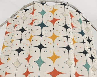 May include: Cream-colored shower curtain with a repeating pattern of starburst shapes in orange, yellow, teal, and black. The design includes small, scattered dots in various colors. The curtain hangs from a curved, silver-colored rod.