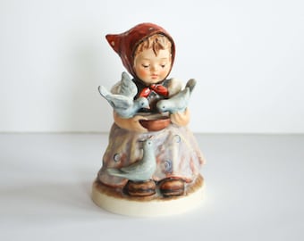 Könnte beinhalten: Eine Porzellanfigur eines Mädchens in einem roten Kapuzenkleid, das drei weiße Tauben aus einer Schale füttert. Das Mädchen lächelt und die Tauben sitzen auf dem Rand der Schale.