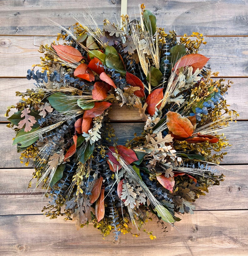 May include: A fall-themed wreath with dried leaves, wheat, and eucalyptus in shades of brown, green, blue, and orange.