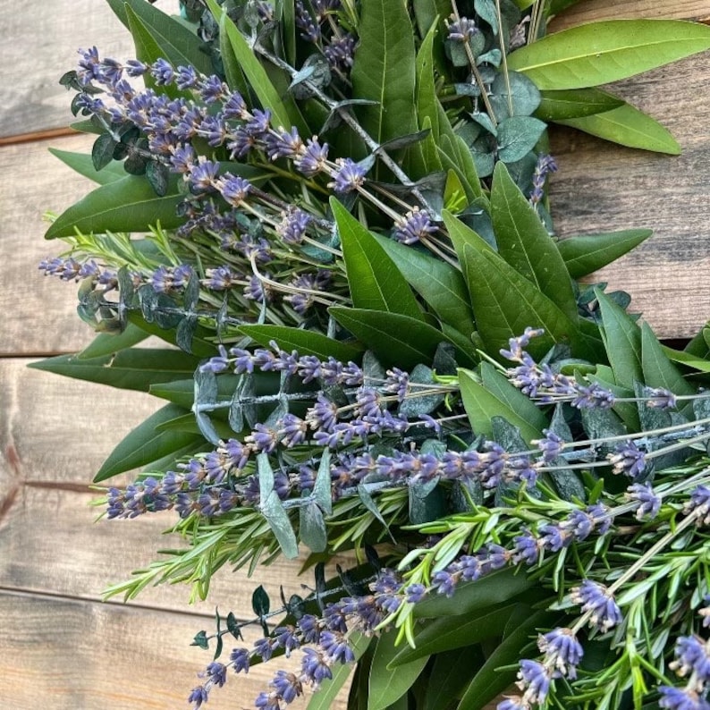 May include: A close-up of a wreath made with lavender, rosemary, and eucalyptus. The wreath is a mix of green and purple hues.