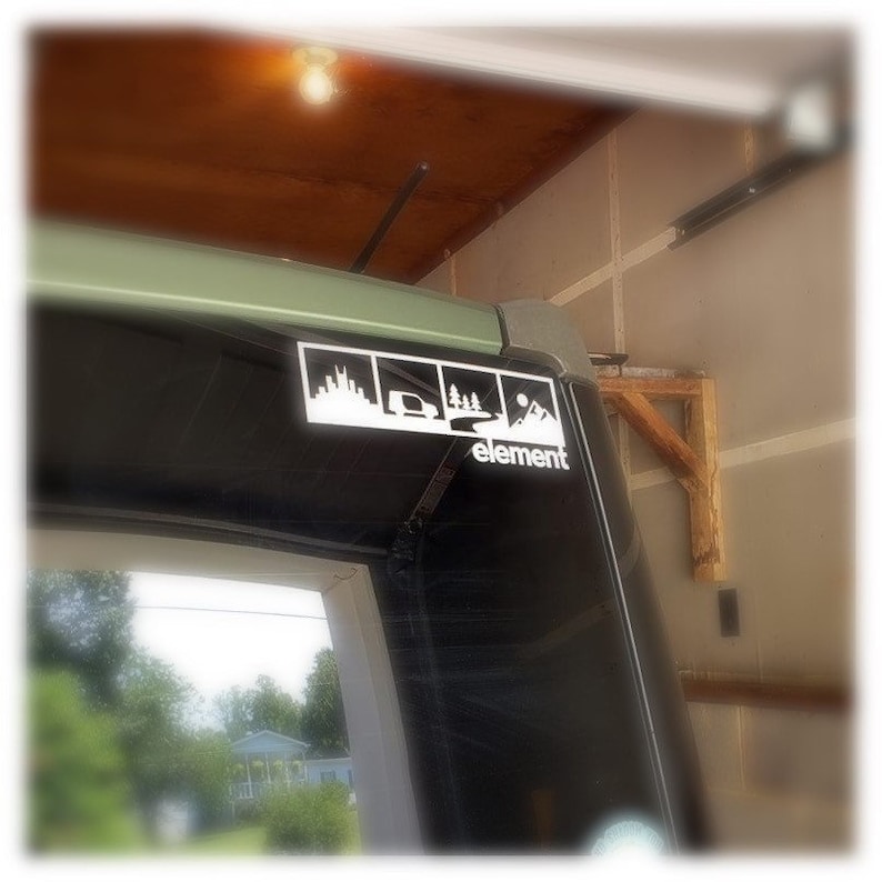 May include: A black car with a white sticker on the back window. The sticker has four images of a city skyline, a car driving on a road, a forest, and a mountain range. The text "element" is below the images.