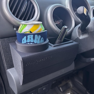 May include: A black matte plastic vehicle dashboard organizer featuring a circular cup holder and a rectangular storage compartment. The organizer is embossed with the text NANO SUPPLY CO and holds a beverage can in a blue foam sleeve.
