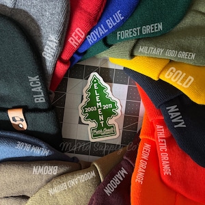 May include: A collection of beanies in various colors, including black, brown, maroon, neon orange, gold, navy, military green, forest green, royal blue, red, and gray. The beanies are arranged in a circle around a sticker with a green pine tree and the text "ELEMENT 2003 2011 Fresh Goods Hand Supply Co."