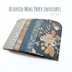 Może przedstawiać: Różne mini koperty papierowe, każda o wymiarach 6,86 cm x 10,16 cm. Koperty mają różne wzory, w tym kwiatowe, w kratę i geometryczne. Kolory obejmują szary, niebieski, brązowy i złoty. Widoczny jest tekst "ASSORTED MINI PAPER ENVELOPES".