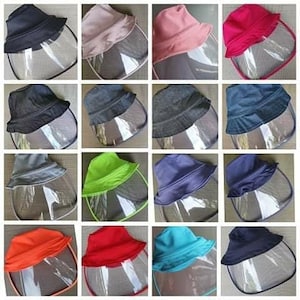 May include: A collection of 10 different coloured bucket hats with a clear plastic face shield attached. The hats are made from various materials, including denim, cotton, and nylon. The face shields are clear and offer protection from the elements.