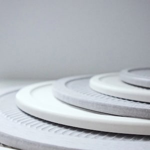 Peut inclure: Un ensemble de quatre sous-verres ronds, gris et blancs, avec une surface texturée. Les sous-verres sont empilés les uns sur les autres.