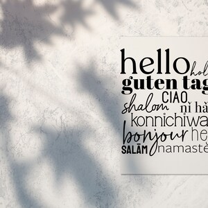 May include: A white card with the words "hello", "guten tag", "hola", "ciao", "shalom", "ni hao", "konnichiwa", "bonjour", "hej", "salām", and "namaste" written in black.
