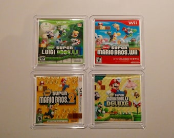 Może przedstawiać: Cztery pudełka z grami wideo z różnymi grami Mario Bros. Pudełka są wykonane z przezroczystego plastiku i pokazują okładki gier. Gry to New Super Luigi U, New Super Mario Bros. Wii, New Super Mario Bros. 2 i New Super Mario Bros. U Deluxe.