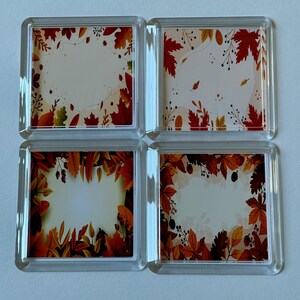 May include: Set of four square glass coasters with an autumn leaf design. The coasters feature a white background with a border of orange, red, and yellow leaves.