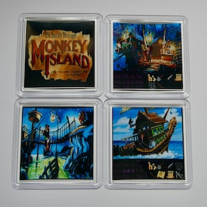 May include: Four square coasters featuring scenes from the video game "Monkey Island." The top left coaster displays the game's logo. The other three coasters depict scenes with characters, buildings, and a ship, all in a vibrant, cartoonish style.