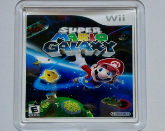 Może przedstawiać: Przezroczysta plastikowa obudowa z wkładką do gry wideo w środku. Gra to Super Mario Galaxy na konsolę Wii. Grafika na okładce przedstawia Mario w kosmicznym otoczeniu z niebieskim tłem i gwiazdami. Gra została oceniona przez ESRB jako E dla wszystkich.