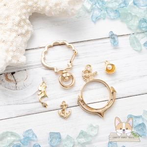 Puede incluir: Un conjunto de dijes de metal dorado con temas náuticos y de sirena. Los dijes incluyen una concha, un ancla, una sirena y un anillo con un diseño de cuerda. Los dijes son perfectos para agregar un toque de fantasía a las joyas o las manualidades.