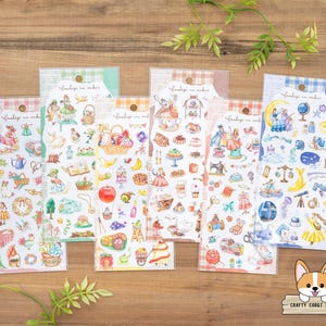 May include: A collection of sticker sheets featuring various whimsical illustrations. The stickers depict scenes with fairies, food, and other decorative elements. Each sheet is packaged in a clear plastic sleeve with a decorative top.