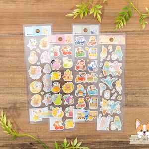 Puede incluir: Tres hojas de pegatinas coloridas con varios diseños de animales y vehículos. Las pegatinas están sobre una superficie de madera. Las pegatinas están en un embalaje de plástico transparente.