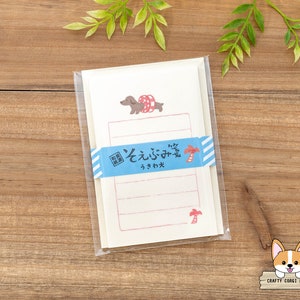 Op de afbeelding: Briefpapier set met een illustratie van een teckel met een zwemband. Het lichtroze papier heeft een blauw-wit gestreepte band en Japanse tekst. De set is verpakt in een transparante plastic hoes.