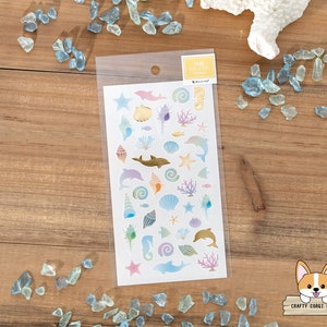 May include: A sheet of colorful stickers featuring a variety of sea-themed designs, including dolphins, seashells, starfish, and coral. The stickers are on a white background and are packaged in a clear plastic sleeve. The text "NB Collection" is printed on the sleeve.