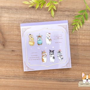 May include: A square, lilac-coloured notepad featuring illustrations of various "mofusand Sanrio characters." The notepad has a decorative border and includes the text "Take a look! Our favourite and precious friends. We are always together!"
