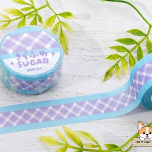 Pode incluir: Um rolo de fita washi azul e roxa com um padr&atilde;o xadrez branco e roxo. A fita tem o texto "Sugar" em japon&ecirc;s e ingl&ecirc;s, e o texto "BGM Inc." no rolo.