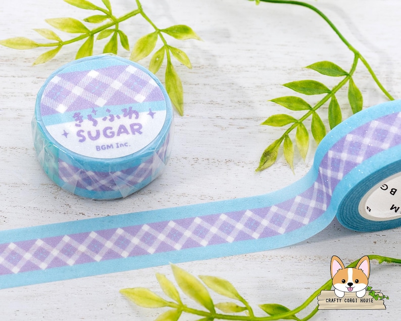 Pode incluir: Um rolo de fita washi azul e roxa com um padr&atilde;o xadrez branco e roxo. A fita tem o texto "Sugar" em japon&ecirc;s e ingl&ecirc;s, e o texto "BGM Inc." no rolo.