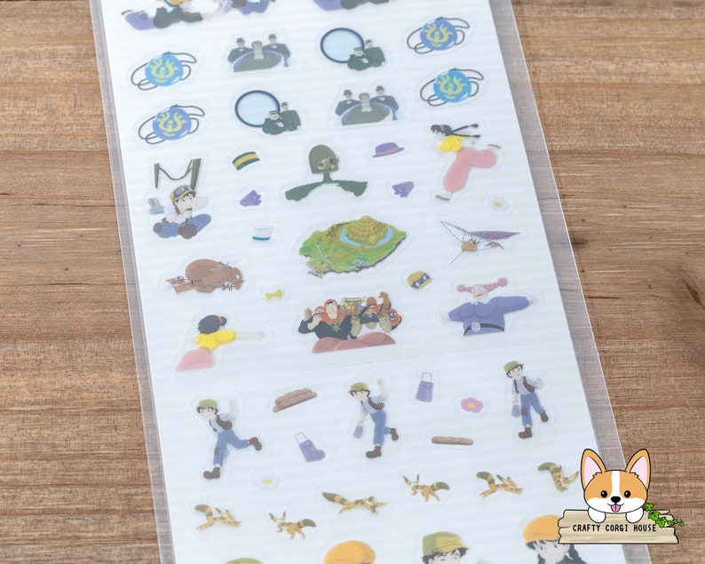 Op de afbeelding: Een vel met transparante stickers met personages en objecten uit de animatiefilm 'Het Kasteel in de Lucht'. De stickers bevatten een meisje met rood haar, een jongen met bruin haar, een vliegtuig, een kasteel en andere fantasierijke ontwerpen.