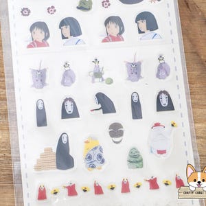May include: A sheet of clear stickers featuring various characters from the animated film, Spirited Away. The stickers include images of Chihiro, No-Face, and other iconic characters in vibrant colors. The stickers are arranged on a white backing.
