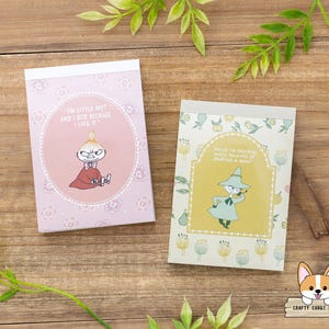 Puede incluir: Dos pequeños blocs de notas con personajes de dibujos animados sobre una superficie de madera. Uno tiene un fondo rosa con el texto "I'M LITTLE MY! AND I BITE BECAUSE I LIKE IT!". El otro tiene un fondo amarillo con un personaje de dibujos animados.