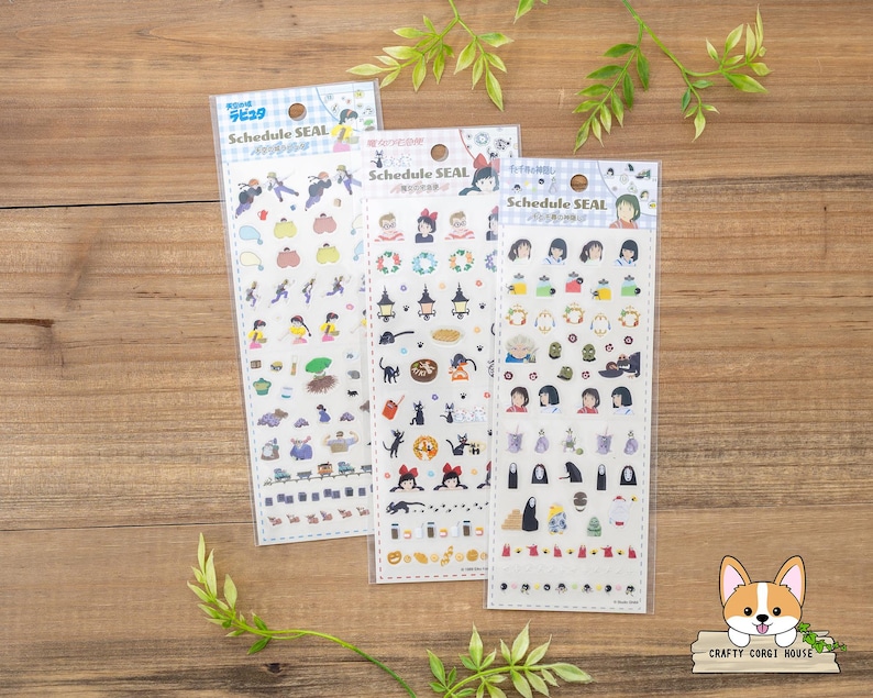 May include: Three sticker sheets with various cartoon illustrations. Each sheet is labeled "Schedule SEAL" and features different characters and objects. The stickers are in clear packaging, and the background is a wooden surface with green leaves.